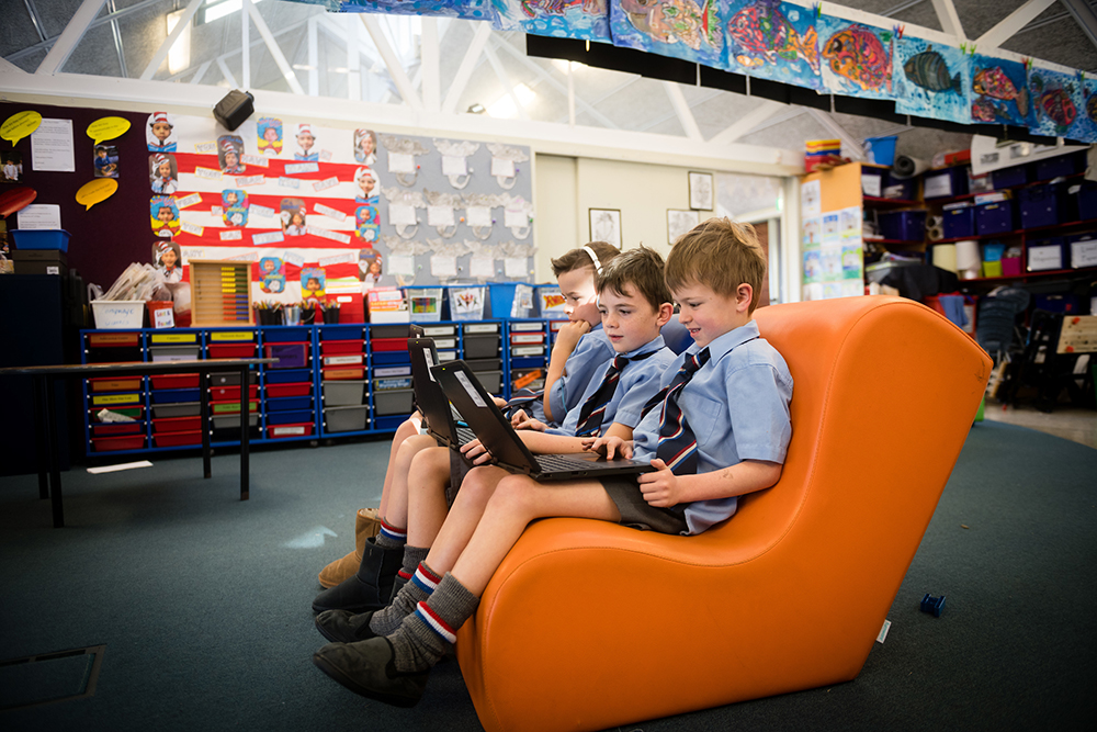 Three boys in a classroom working together on a laptop