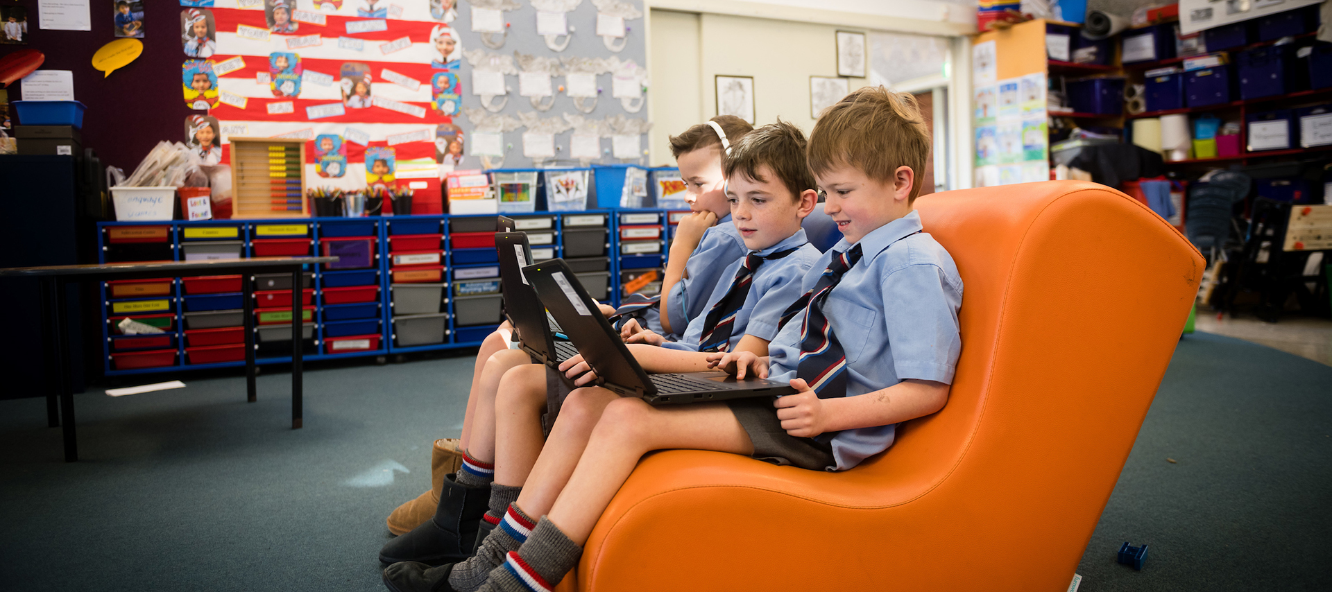 Three boys in a classroom working together on a laptop