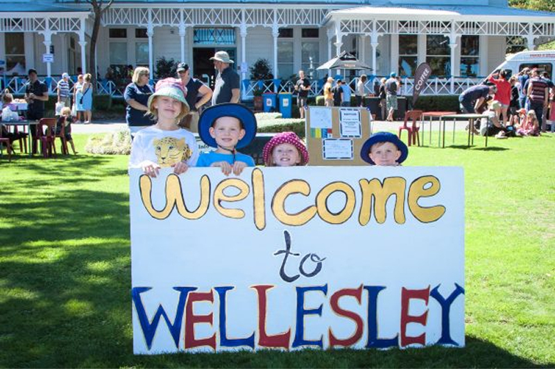 Four children in front of Days Bay House holding a ‘Welcome to Wellesley’ sign