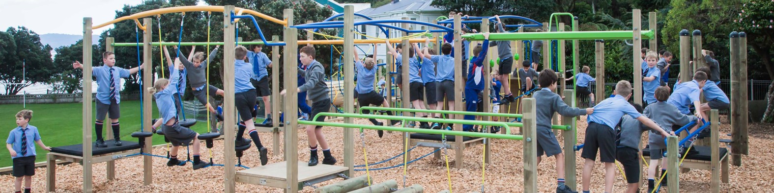 A few students in school uniforms playing on a playground, with trees and greenery in the background