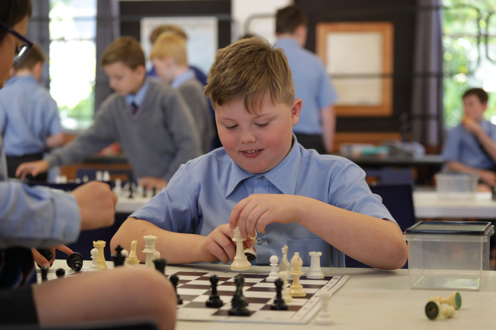 Wellesley sctudent in school uniform smiling and enjoying a game of chess, seated at a chessboard with pieces in mid-play