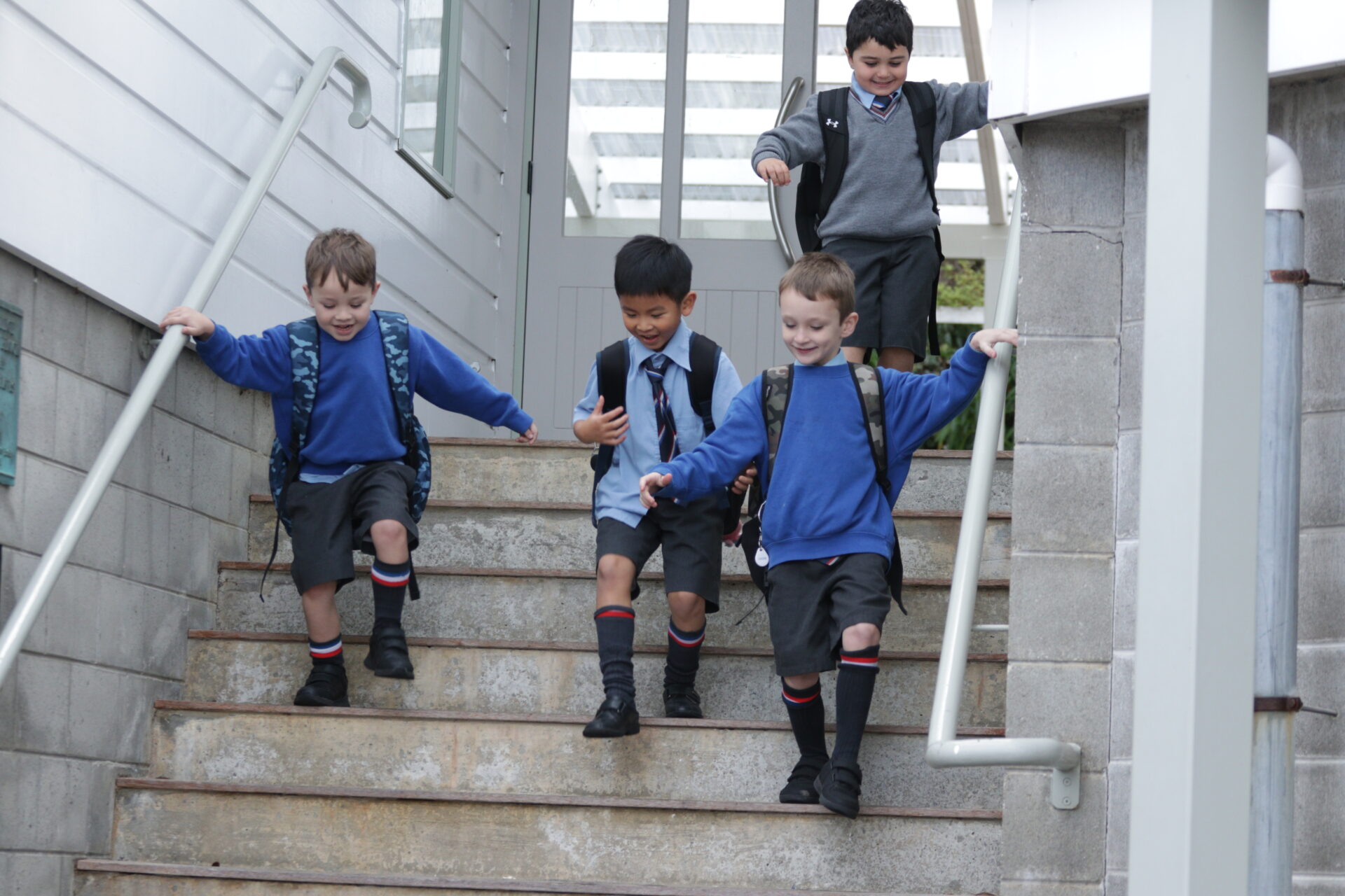 Four Wellesley College boys in school uniforms walking down stairs with their school bags