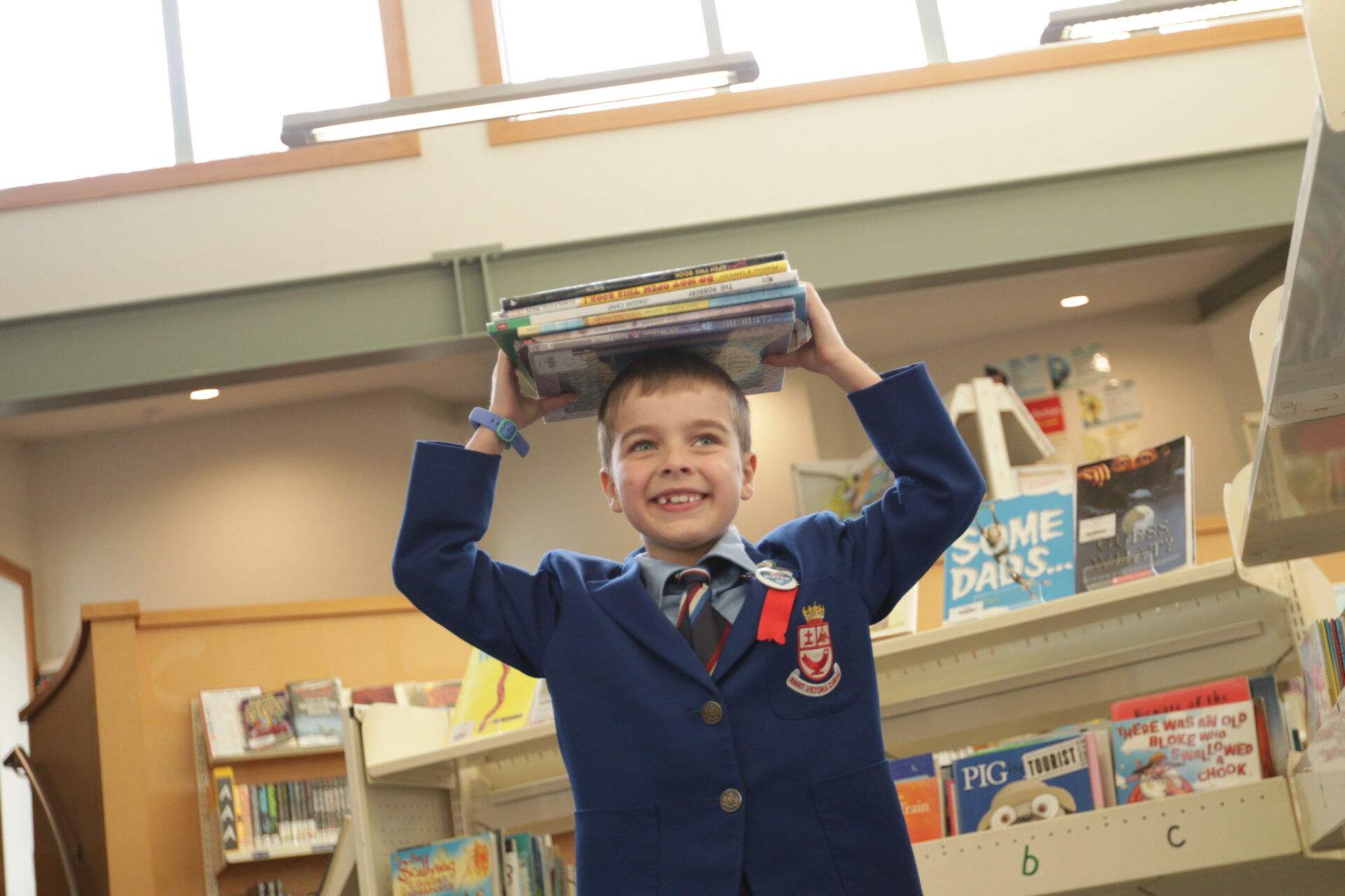 A happy Wellesley boy in the library balancing a book on his head and smiling playfully